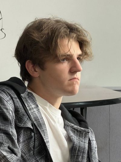 A teenage boy in a plaid jacket and white t-shirt sits in profile, his expression serious and inward, waiting between takes on set.