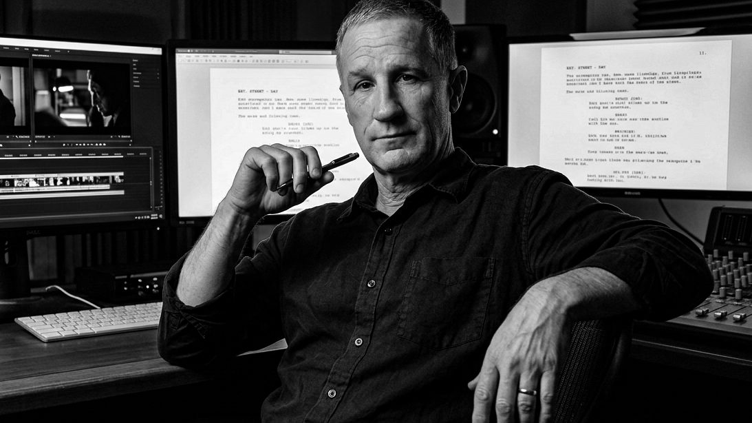 Writer and director Daniel J Lennox at a desk, writing beside two monitors.