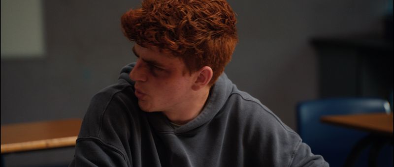 A teenage boy in profile, turning to look behind him.